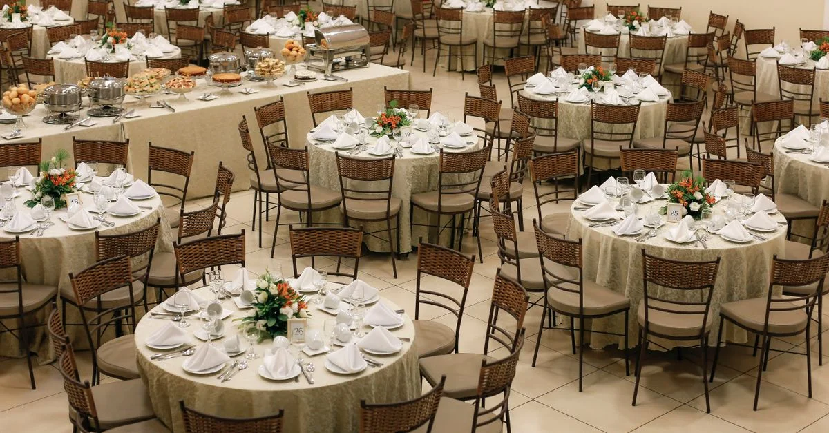 Une salle de banquet spacieuse, aménagée avec des tables rondes soigneusement disposées et des centres de table floraux, est prête pour un grand événement.