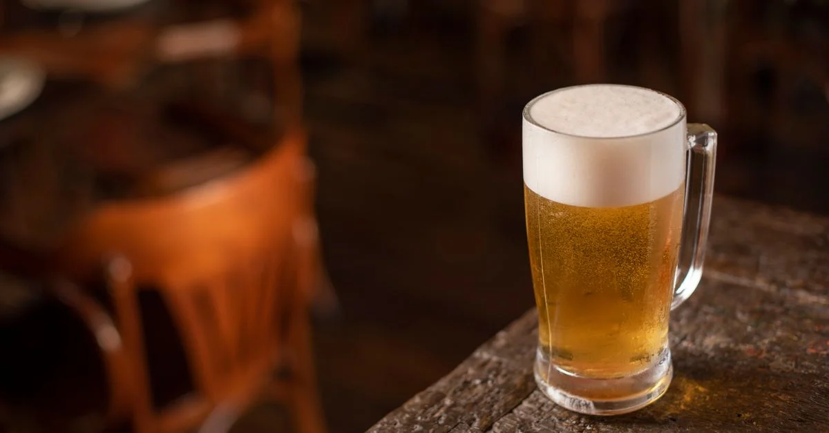 Gros plan sur une chope de bière mousseuse sur une table en bois dans une ambiance de pub confortable.