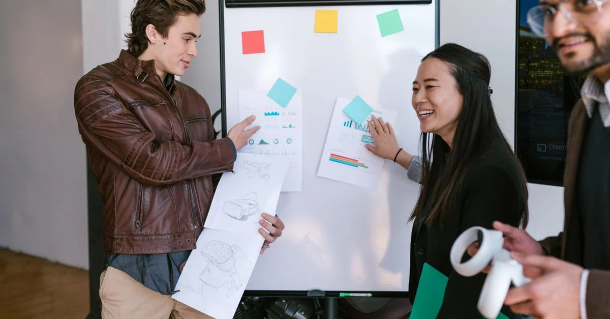 Équipe multiculturelle collaborant et partageant des idées sur une présentation commerciale avec graphiques et tableau blanc.
