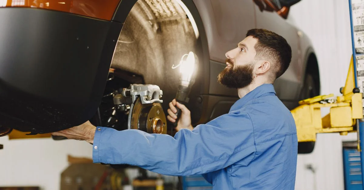 Mécanicien professionnel en bleu de travail inspectant les freins d'une voiture dans un garage bien éclairé.
