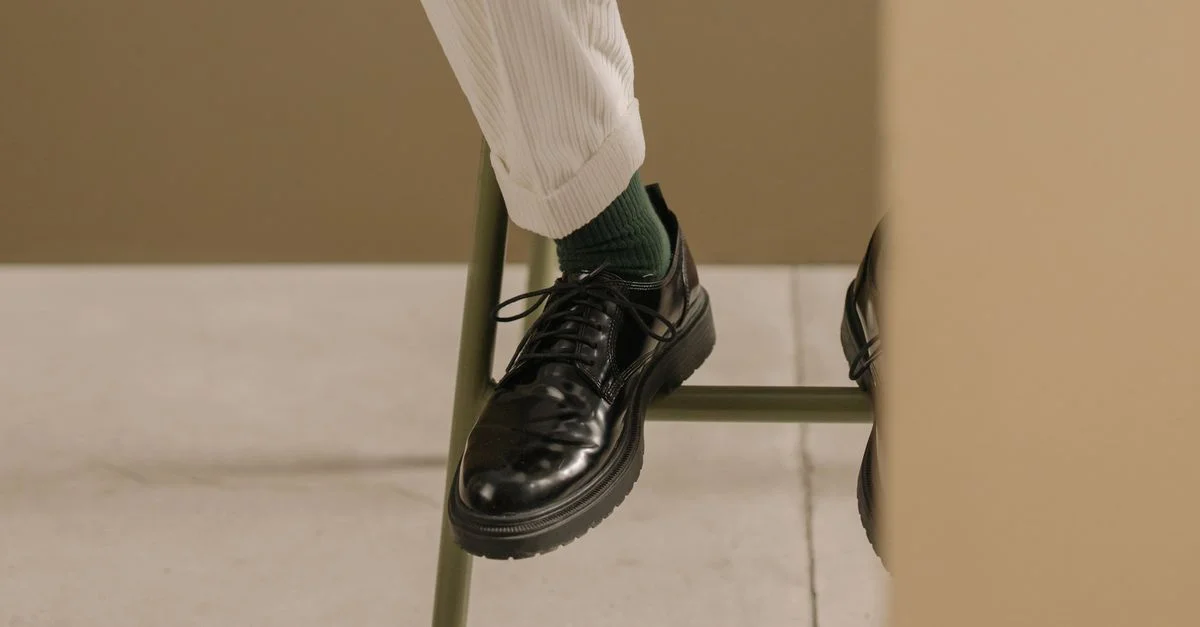 Gros plan sur des chaussures en cuir noir élégantes associées à des pantalons blancs, mettant en avant un style chic et moderne.