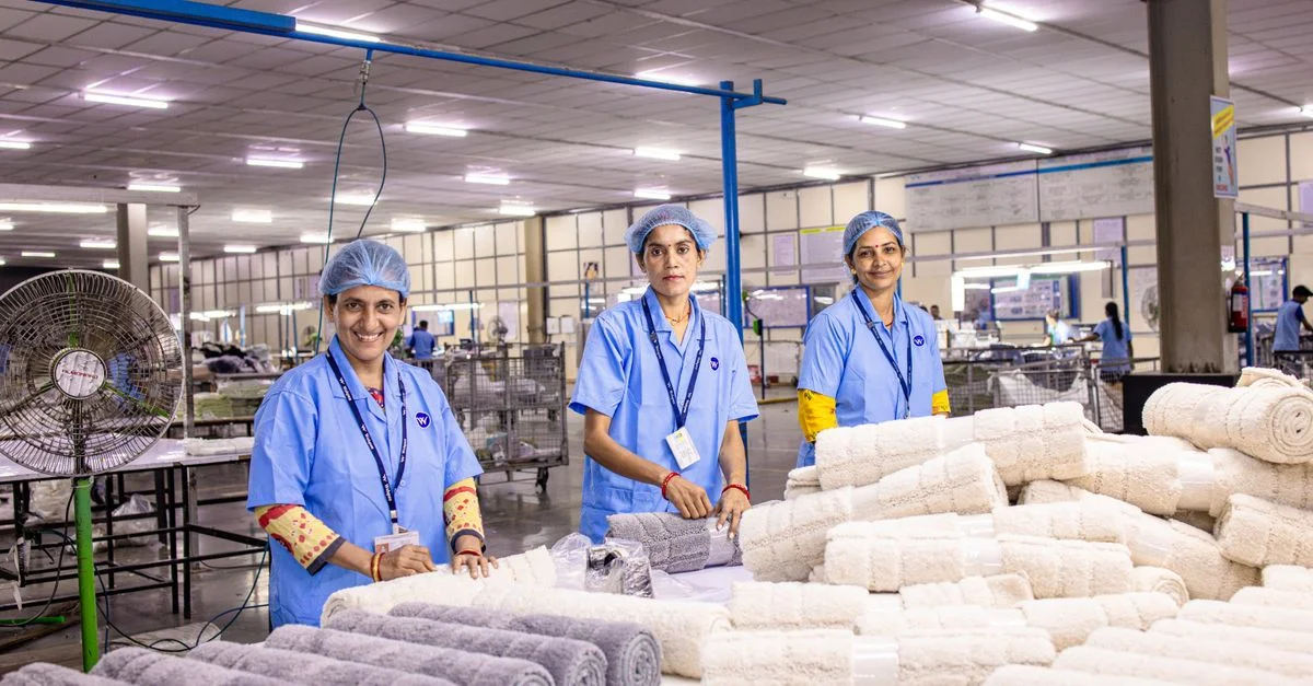 Trois travailleuses en uniforme bleu pliant des serviettes dans une usine textile.