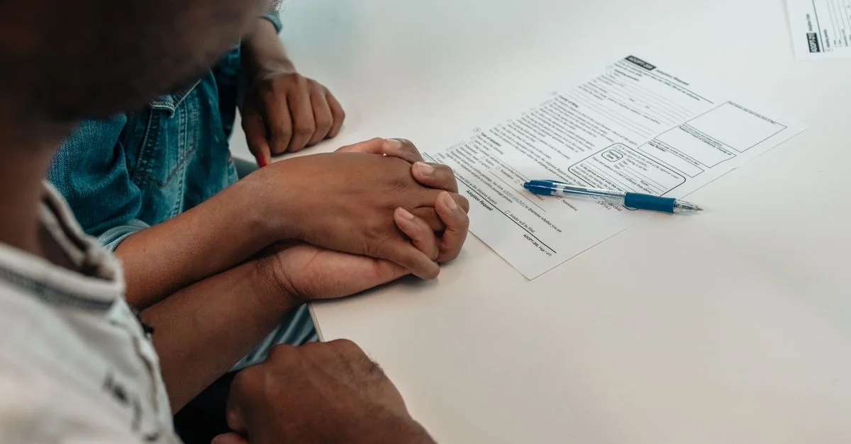 Une famille se soutient mutuellement pendant le processus d'adoption, tenant des mains au-dessus de documents importants.