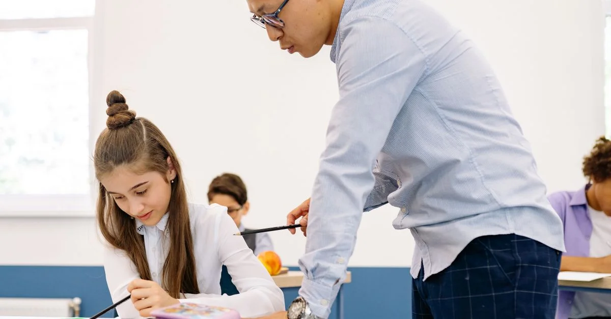 Un enseignant asiatique aidant une jeune fille caucasienne dans ses études dans un cadre de classe.