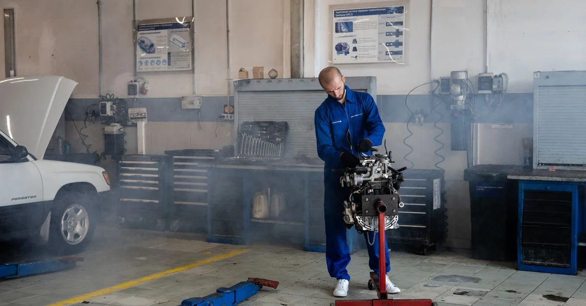 Un mécanicien réparant un moteur de voiture dans un atelier de réparation automobile occupé avec des outils autour.