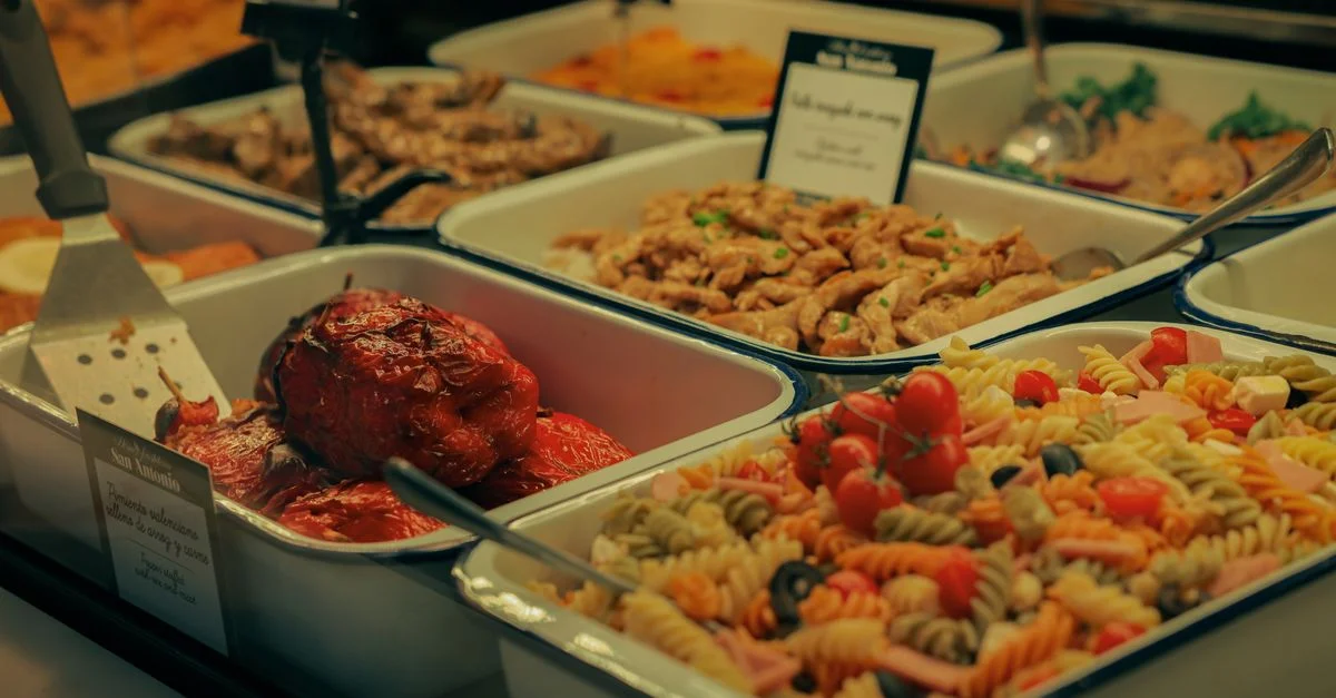 Un buffet varié comprenant une salade de pâtes, des viandes et des poivrons farcis.